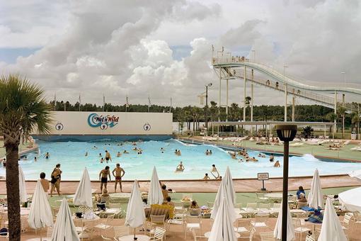 Color photo of an aqua park in Florida with swimming pool, water slide, in the foreground a terrace with white garden furniture and umbrellas