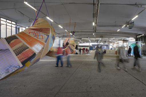 Ausstellungsansicht mit in einer bunten Installation, die sich wie eine Schachtelkette durch eine Halle schlängelt