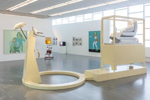 Exhibition view: painting on white background, in the foreground a group of sculptures