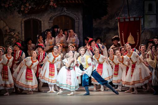 Photo of numerous dancers in folk costumes in white and red, in the foreground the soloist couple