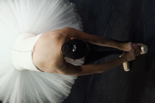 Photo of a ballerina in a white tutu leaning forward to her ballet shoes, top view