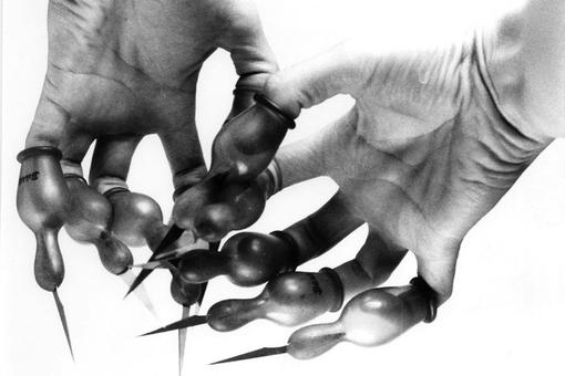 Close-up in black and white of two hands: pacifiers with extremely sharp knife tips at the end are placed over the fingers