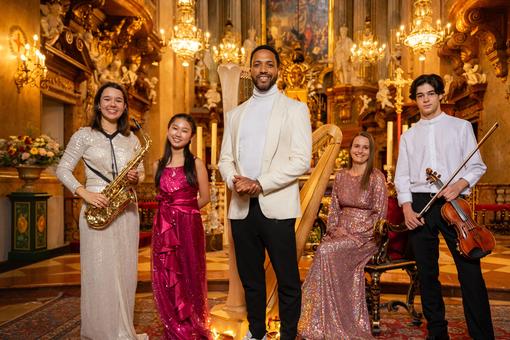 The photo shows the artists of the Christmas concert: two men and three women in festive dress inside a baroque church