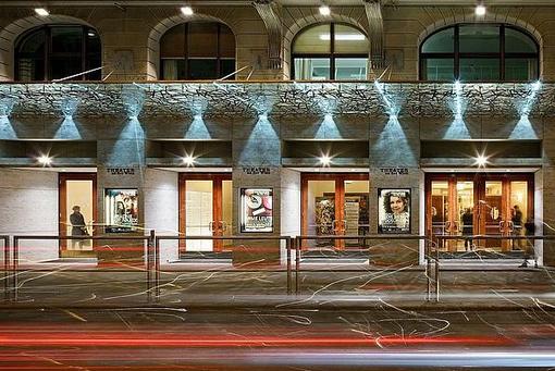 You can see the entrance area of the Theater an der Wien, in evening lighting and some people in front of the entrance doors