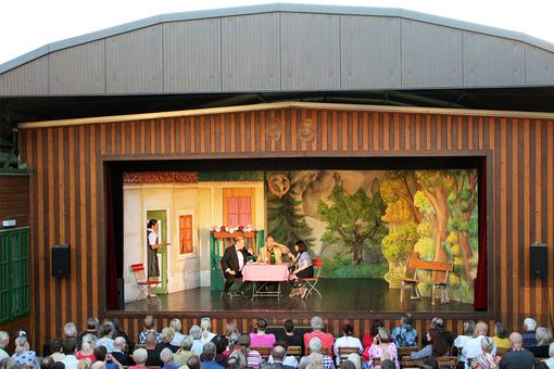 Stage view of the open air stage, 4 actors in a scene in a typical Austrian restaurant garden, in front of the stage the audience