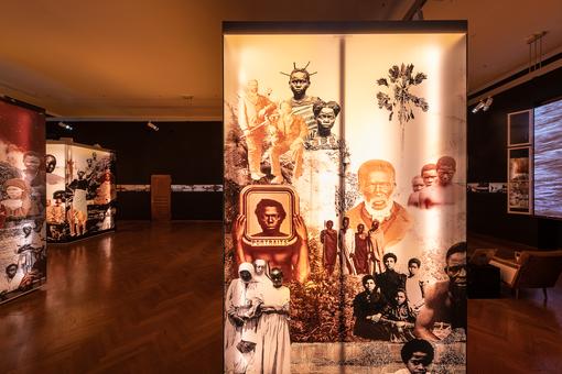 Exhibition view with backlit images of various indigenous peoples