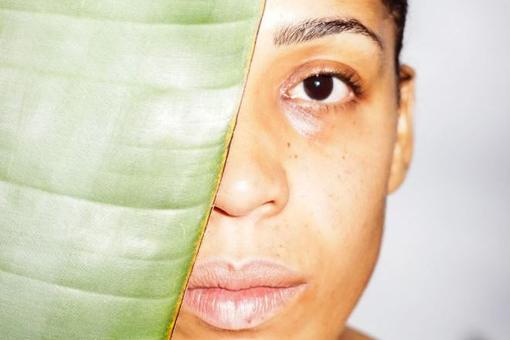 The photo shows the face of a young woman with dark eyebrows and dark hair, half of her face is covered by a large leaf