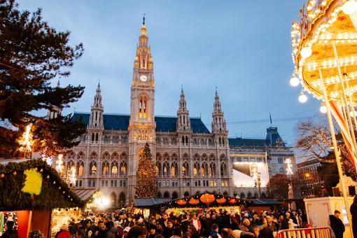 Das Foto zeigt das bunte Treiben am Wiener Christkindlmarkt auf dem Rathausplatz, die beleuchteten Hütten, im Hintergrund das Wiener Rathaus