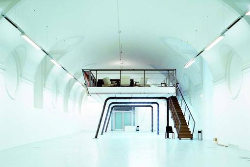 Interior view of designforum Wien: elongated, upward-arched room with a suspended metal gallery containing a seating area and reached via a freestanding staircase