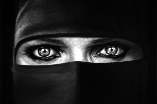 Black and white picture showing a pair of eyes, very expressive eyes, the rest of the face is covered with black fabric